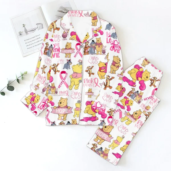 The Winnie Pooh Pink Power satin pajamas styled in a flat lay on a white surface with a book and a small green sprig.