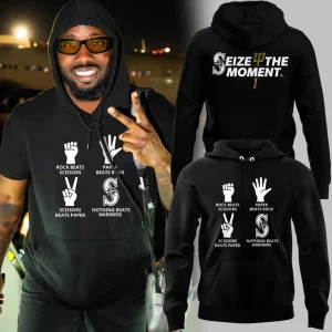 Person wearing Seattle Mariners Paper Beats Rock hoodie, front graphic visible, nighttime backdrop.